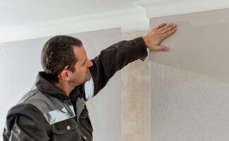 Man glues gray vinyl wallpaper on a backing. Renovation of the room, wall repairman is finishing wallpapering