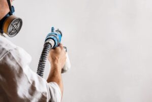 Worker painting wall with spray gun in white color. Copy space.